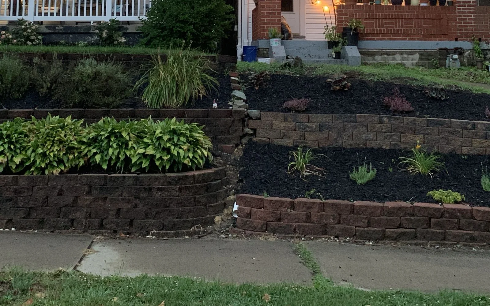 Wide view of terraced front-yard garden beds with black mulch and young plantings in Pittsburgh, Pennsylvania